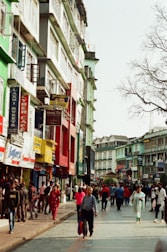 A vibrant neighborhood street with families walking and local shops bustling under a clear sky.
