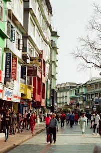 A vibrant neighborhood street with families walking and local shops bustling under a clear sky.