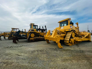 A fleet of bulldozers leveling ground under a clear blue sky.