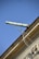 An ornate drainpipe extends from the corner of a building, supported by intricate wrought iron brackets. The architectural details include decorative elements at the base. The sky is bright and clear, providing a striking contrast to the building's structure.