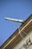 An ornate drainpipe extends from the corner of a building, supported by intricate wrought iron brackets. The architectural details include decorative elements at the base. The sky is bright and clear, providing a striking contrast to the building's structure.