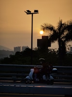 A delivery person navigating through city streets on a scooter during sunset.