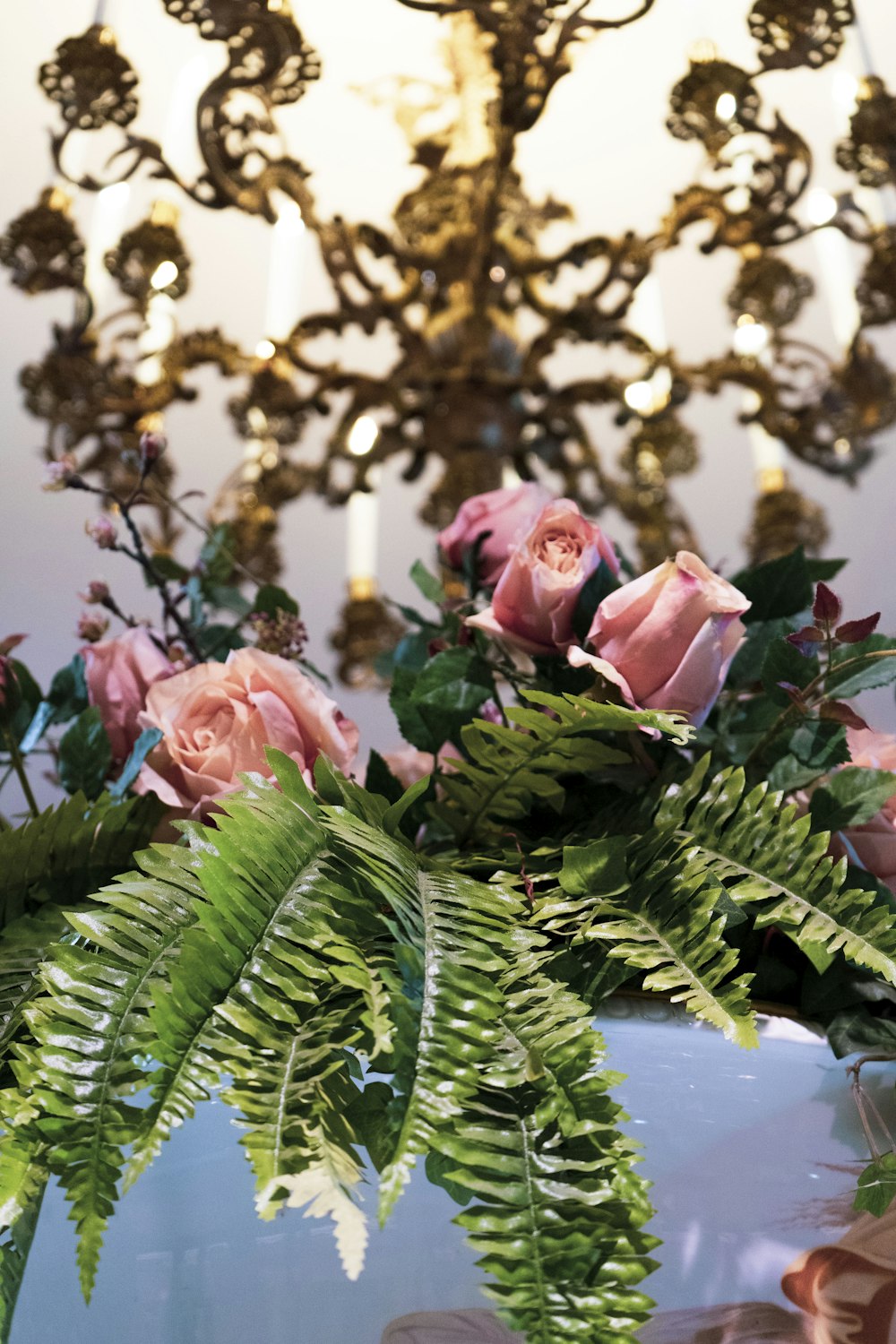 a chandelier with pink roses and ferns in it