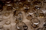 A collection of clear glass bottles and decanters with gold accents arranged closely together, showcasing intricate craftsmanship and symmetry.