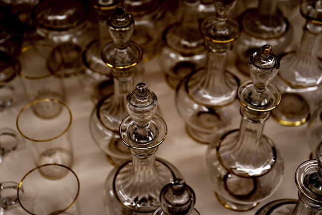 A collection of clear glass bottles and decanters with gold accents arranged closely together, showcasing intricate craftsmanship and symmetry.