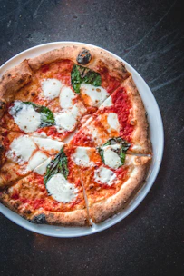 A crispy golden pizza topped with fresh tomatoes, basil, and mozzarella.
