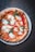 A round pizza topped with melted mozzarella cheese, fresh basil leaves, and tomato sauce, served on a white plate. The crust is well-baked with a golden-brown hue.