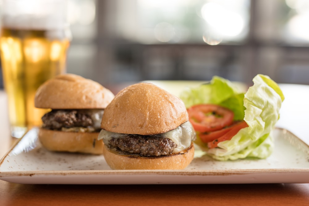 two hamburgers on a plate with lettuce and tomato