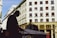 A silhouette of a person, possibly a coach driver, is visible in the foreground while in the background there is a large, white multistory building with multiple windows and the name 'Raiffeisenbank' is prominently displayed.