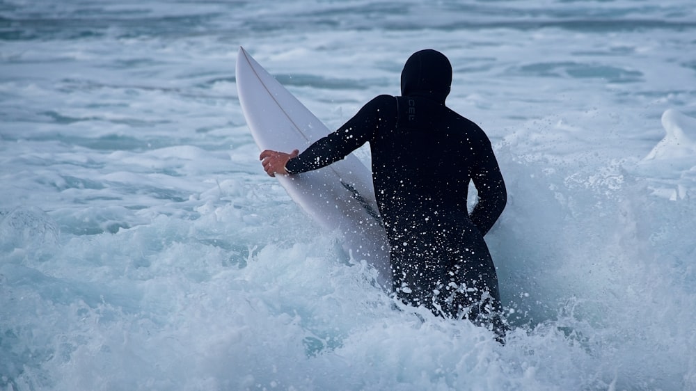 a man in a black wet suit holding a white surfboard
