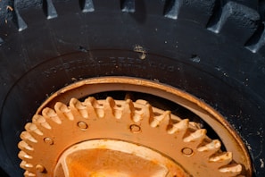 Close-up view of a large, heavy-duty tire with deep treads, featuring a prominently visible rim and hub in an orange hue. The text 'Industrial Deep Lug' is embossed on the rubber surface of the tire, indicating its specialized design for industrial use. Signs of wear and minor scratches are apparent on the metallic parts.