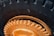 Close-up view of a large, heavy-duty tire with deep treads, featuring a prominently visible rim and hub in an orange hue. The text 'Industrial Deep Lug' is embossed on the rubber surface of the tire, indicating its specialized design for industrial use. Signs of wear and minor scratches are apparent on the metallic parts.