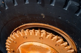Close-up view of a large, heavy-duty tire with deep treads, featuring a prominently visible rim and hub in an orange hue. The text 'Industrial Deep Lug' is embossed on the rubber surface of the tire, indicating its specialized design for industrial use. Signs of wear and minor scratches are apparent on the metallic parts.