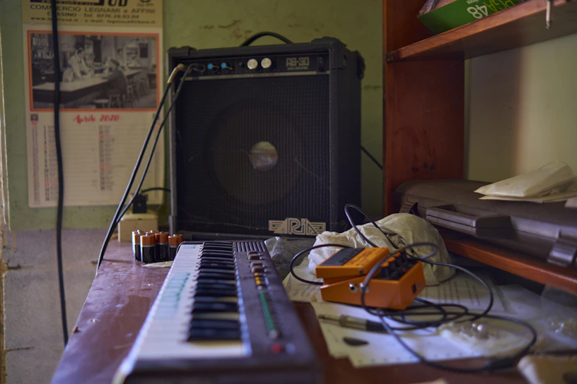 A cozy home studio with a guitar, keyboard, and music sheets scattered on a wooden desk.