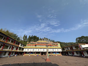 A serene Himalayan monastery courtyard bathed in early morning light, with monks engaged in lively philosophical debate.