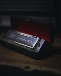 An elegant harmonica rests in its open black case, which has a red interior. The harmonica's metallic surface catches the light, highlighting its polished finish and embossed branding. The scene is set on a wooden surface, creating a warm, rustic ambiance.
