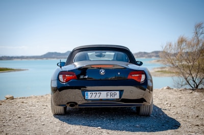 A sleek black convertible parked along a sunny Southern California coastline at sunset.