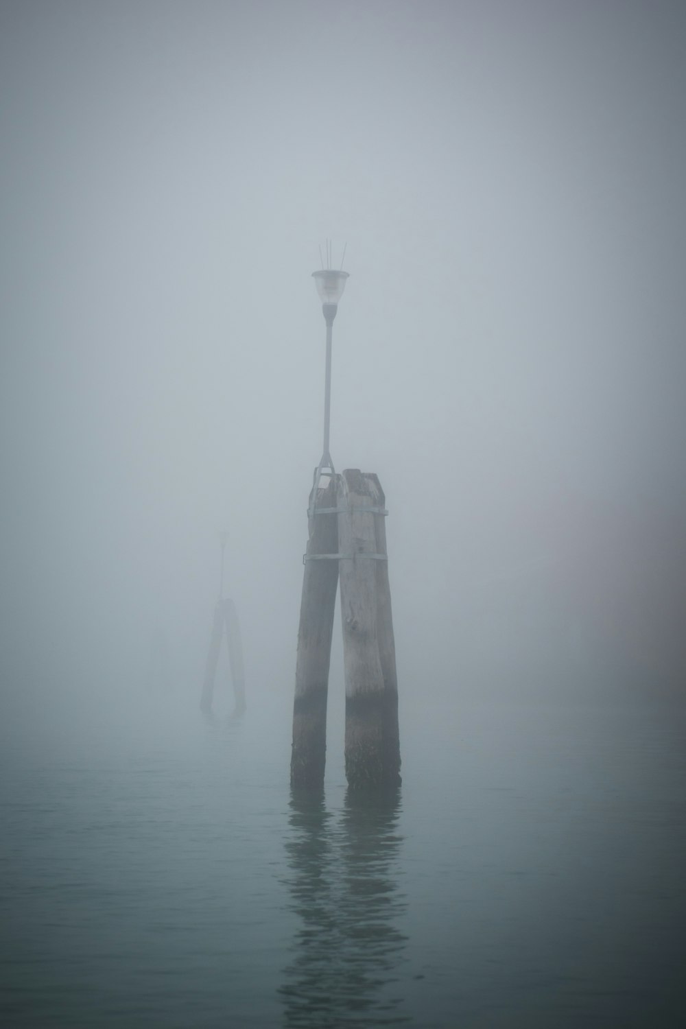 a foggy day with a light pole in the middle of the water