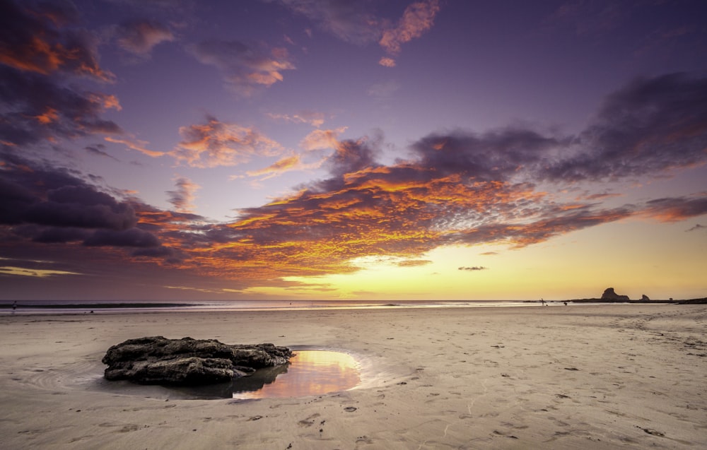 Una puesta de sol en una playa con una roca en primer plano