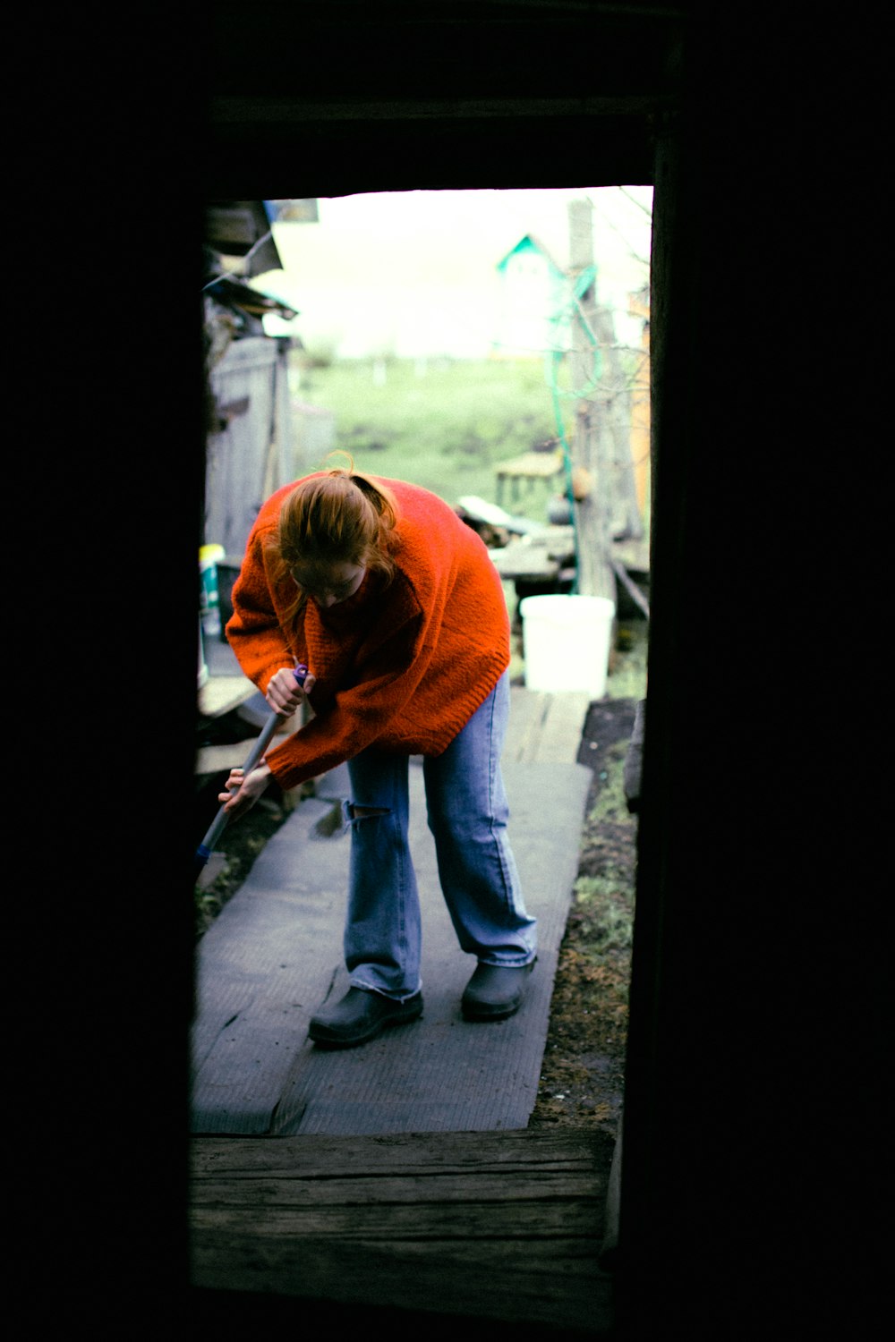 a woman in an orange sweater cleaning a porch