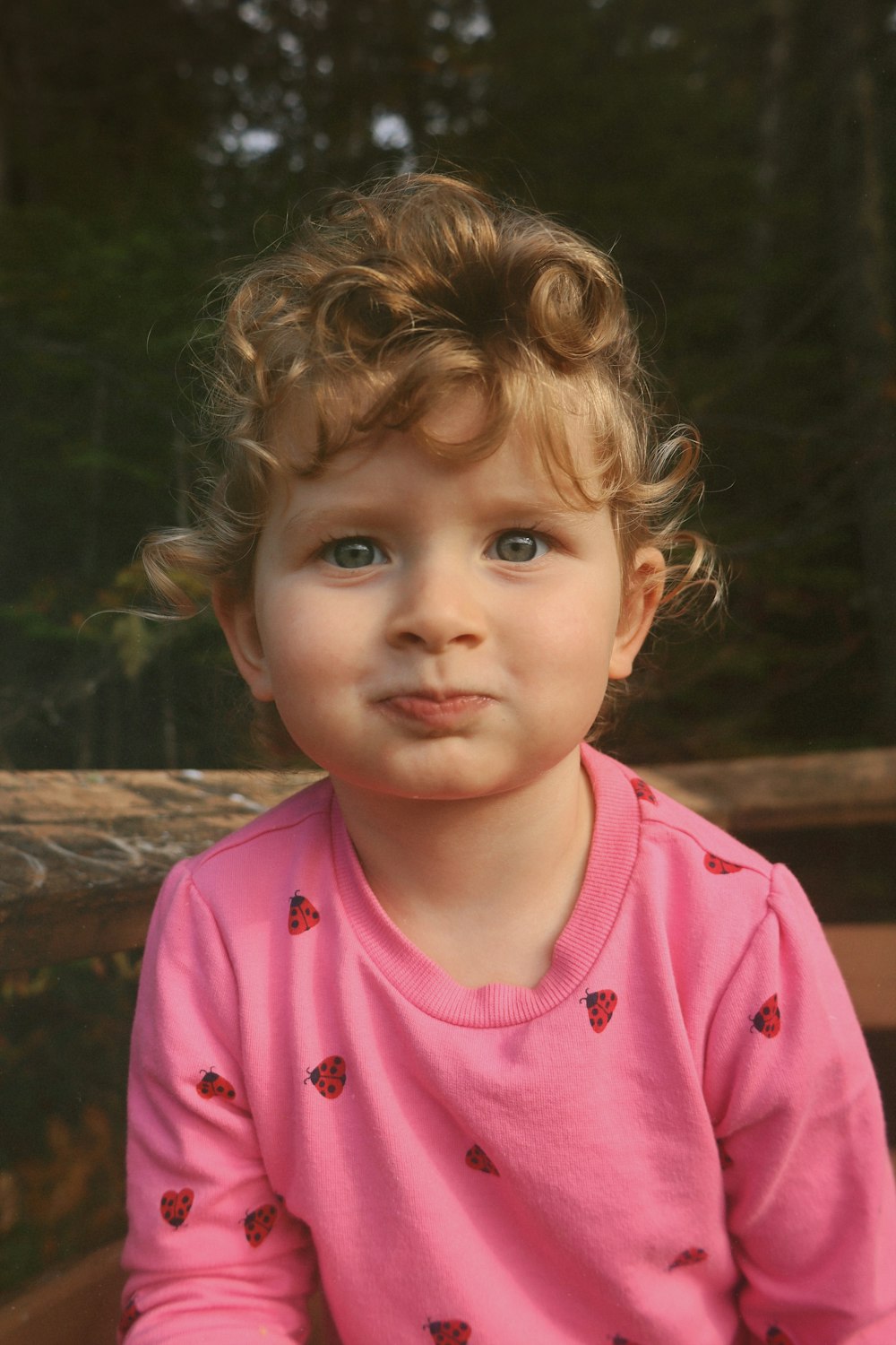 a little girl in a pink shirt sitting on a bench