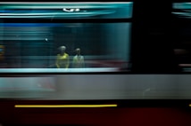Mannequins in yellow clothes appear behind a blurred motion effect that likely suggests the framing of a moving vehicle or train. The scene creates a surreal and ghostly atmosphere, blending a static fashion display with dynamic motion.