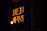 A bright neon sign with the word JEJU and Korean characters glows in a warm orange color, partially reflected in the window with a dark background.