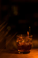 A stylish glass filled with amber liquor and ice cubes, glowing softly under subtle gray and orange lighting.