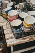 A collection of colorful handmade mugs arranged on a rustic wooden table.
