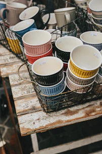 Brightly colored hand-thrown ceramic mugs arranged on a wooden table with natural light.