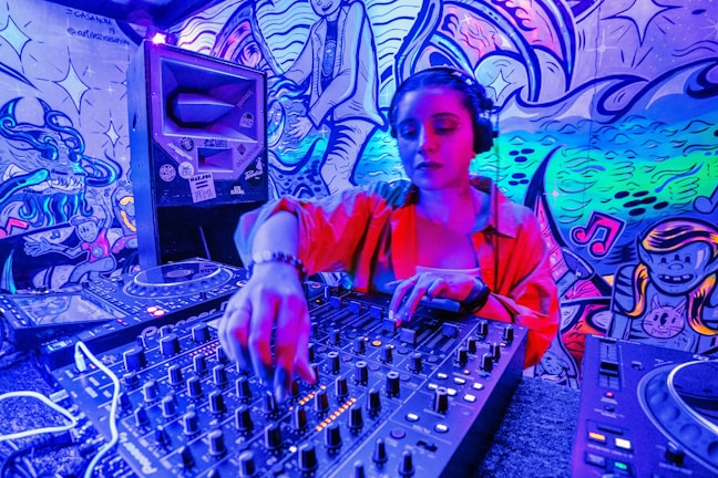 A DJ wearing headphones operates a sound mixer in a vibrant, graffiti-decorated environment. The scene is illuminated with neon lights, creating a vivid blue and pink hue. The graffiti on the walls features artistic and musical imagery.