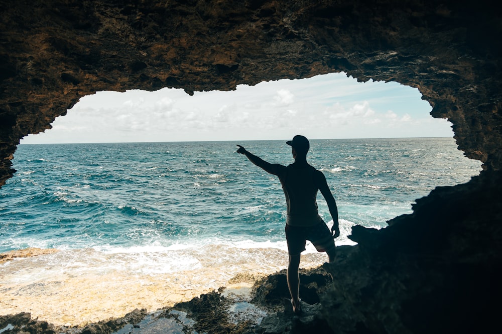 um homem de pé em uma praia rochosa ao lado do oceano