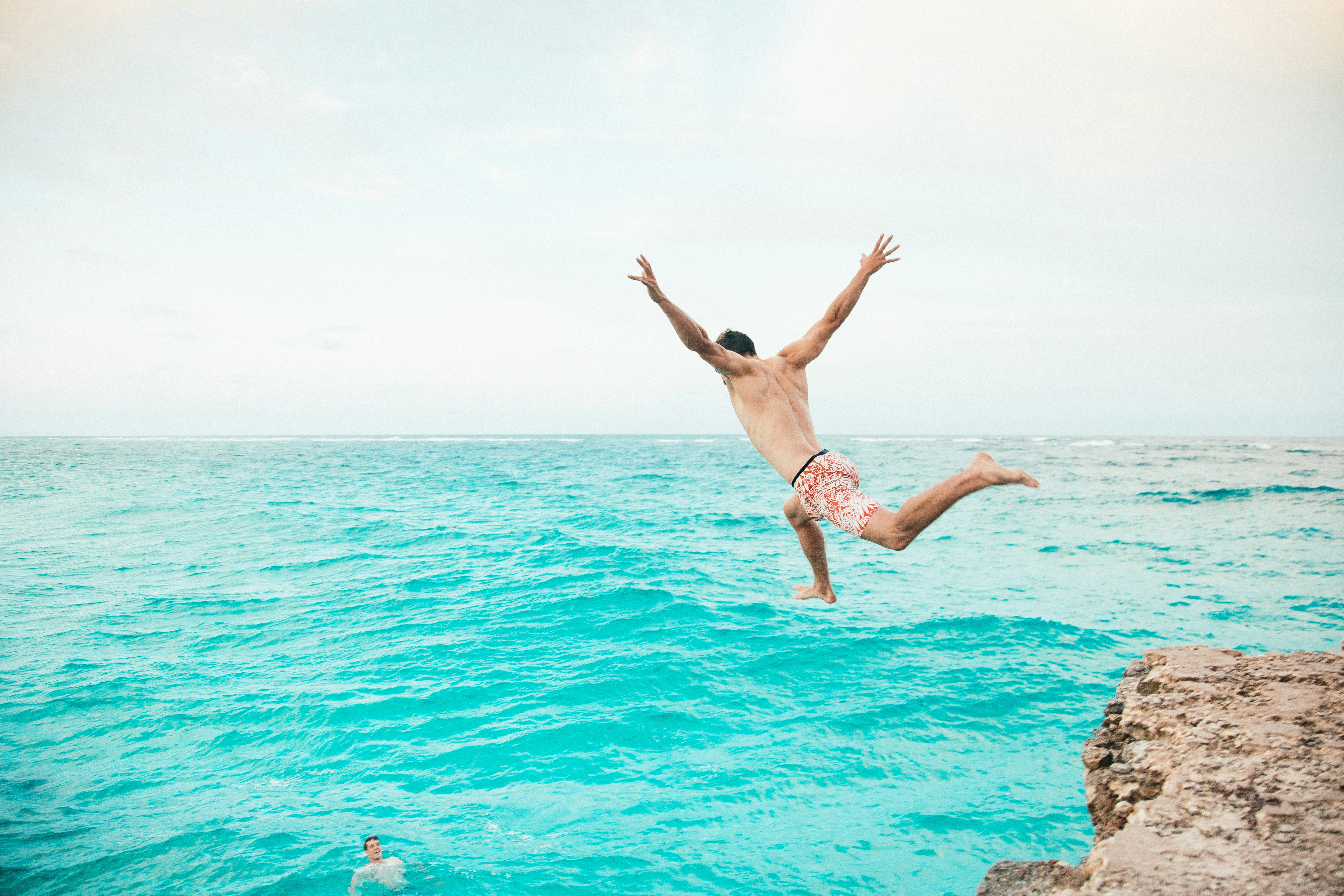 A man jumping off a cliff into the ocean photo Free Barbados Image on