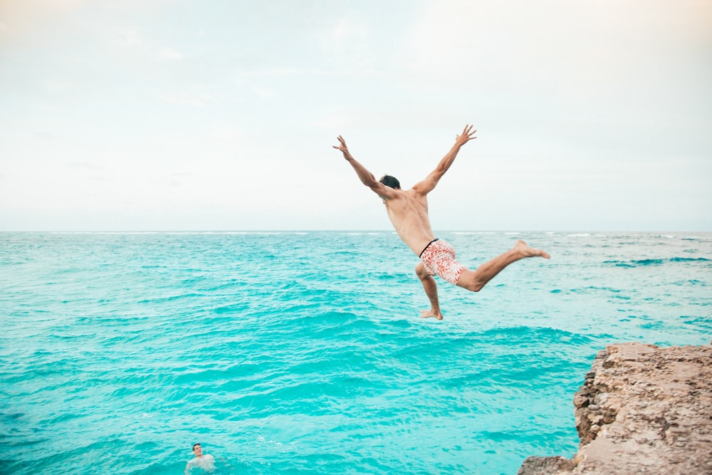 a man jumping off a cliff into the ocean