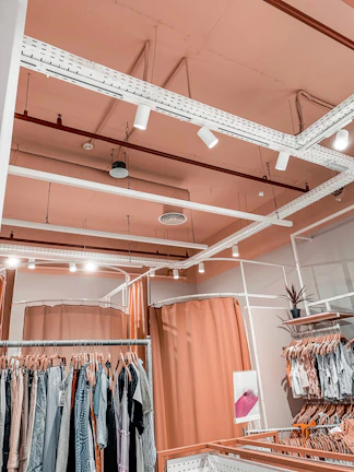 Interior view of a modern, cozy women's clothing shop with rose and white decor and happy customers browsing