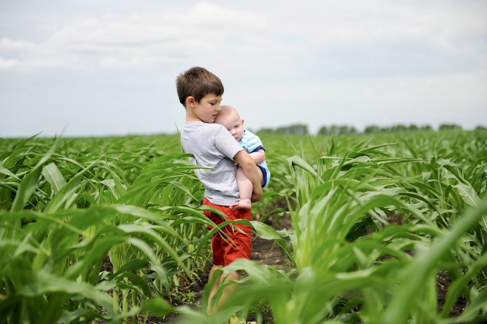 a young boy holding a baby in a field