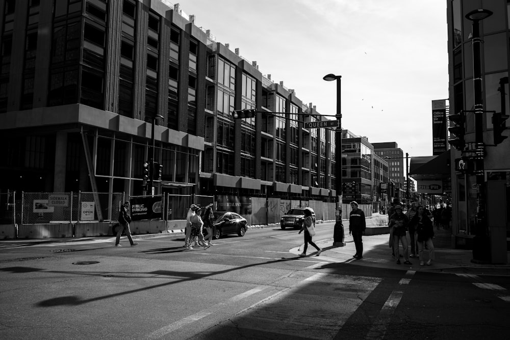 a group of people walking across a street next to tall buildings