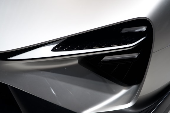 A close-up view of a modern car headlight, featuring sleek lines and a futuristic design. The light assembly is integrated into a metallic silver body with sharp angles, contributing to a high-tech aesthetic.
