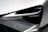 A close-up view of a modern car headlight, featuring sleek lines and a futuristic design. The light assembly is integrated into a metallic silver body with sharp angles, contributing to a high-tech aesthetic.