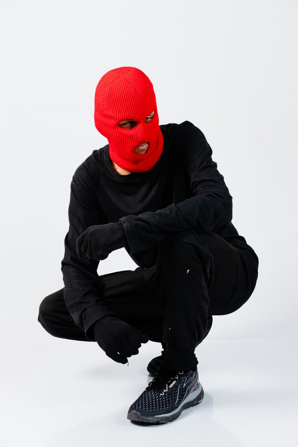 Un homme au masque rouge accroupi sur fond blanc