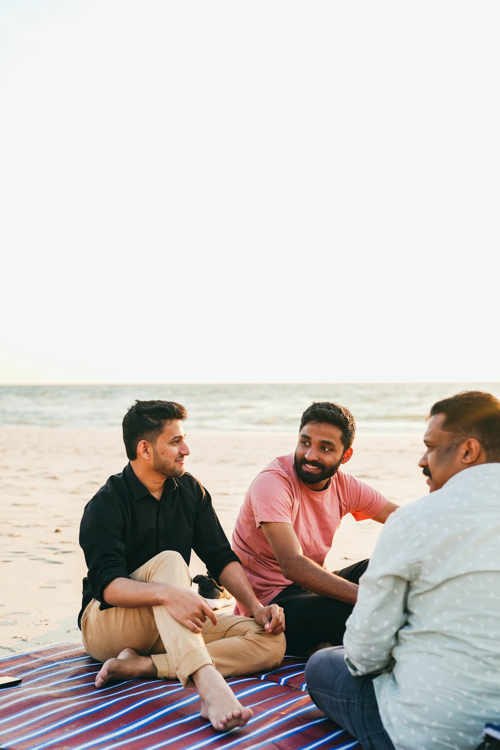 a group of men sitting on top of a beach next to the ocean
