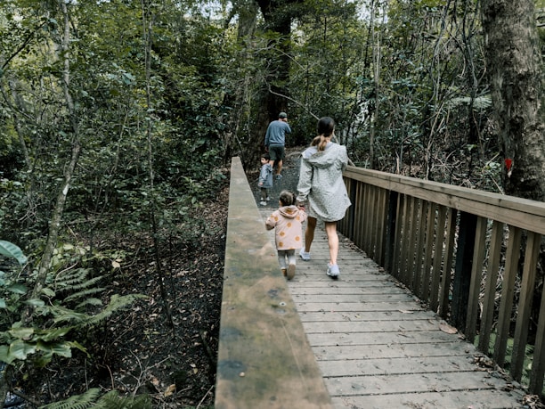 A group of trekkers crossing a wooden bridge surrounded by lush green forest.