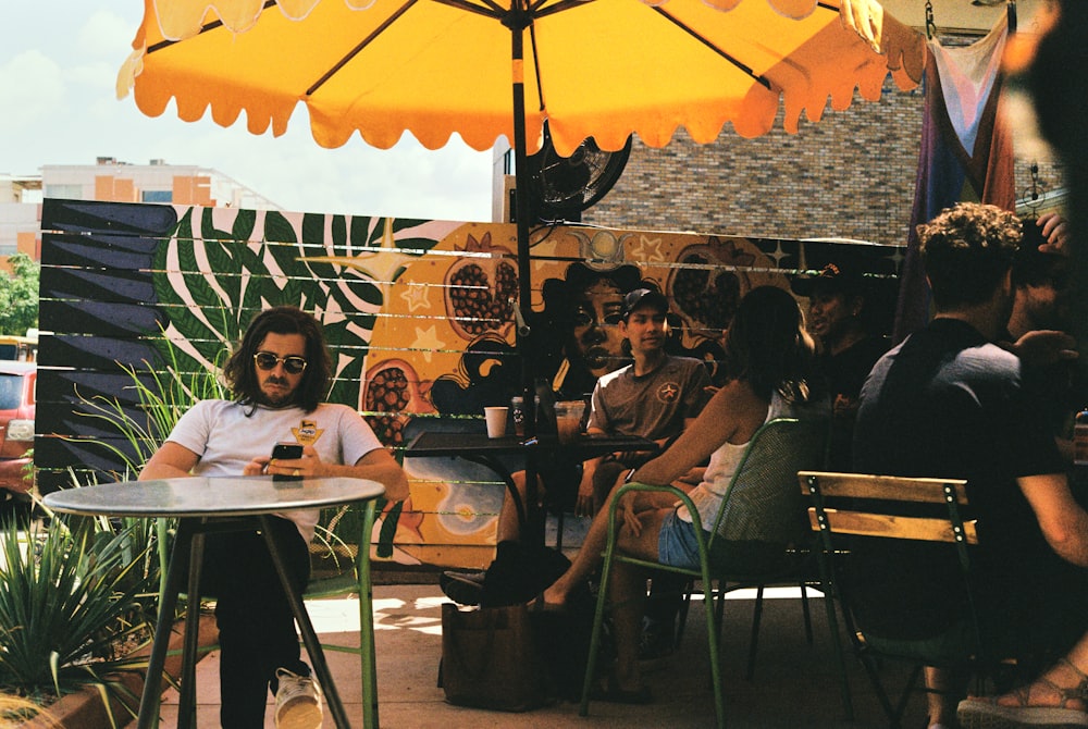 a group of people sitting around a table under an umbrella