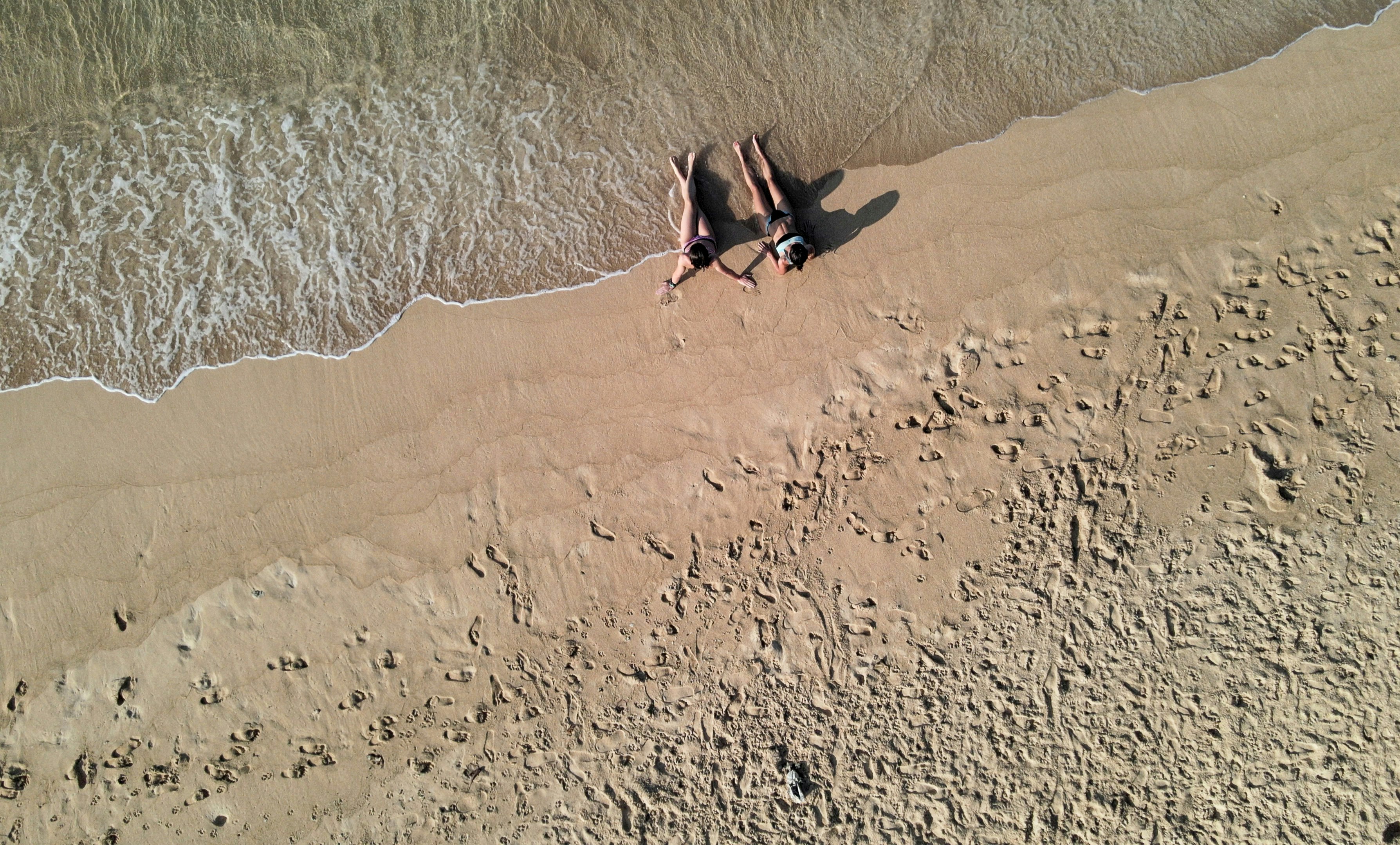 Zwei Personen liegen im Sand an einem Strand