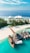 A tropical island features pristine white sandy beaches, lush green palm trees, and turquoise blue waters. A group of traditional wooden boats and a small yacht are docked at a wooden pier. In the background, a luxury resort with white tent-like structures is visible on the water.