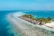 A serene tropical scene featuring overwater bungalows lined along a pristine beach with clear turquoise waters. Lush palm trees accompany the bungalows, creating a picturesque and tranquil vacation setting. The ocean extends into the horizon, displaying vibrant shades of blue and creating a perfect backdrop.