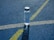 A clear plastic water bottle labeled H2O stands upright on a textured blue surface, intersected by white and yellow lines, likely part of a sports track.