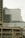 A modern multi-story office building with a white and glass facade, including a domed section at the top. Multiple flags are visible on the lower part of the building. In the foreground, there is a concrete parking structure with multiple levels, including visible vehicles.