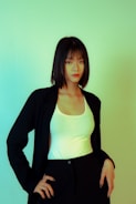 A person with short, dark hair is wearing a black jacket over a white top. The background is a gradient of green and yellow tones.