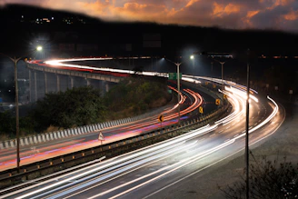 A dynamic highway at dusk illuminated by streaks of fast-moving headlights symbolizing speed.